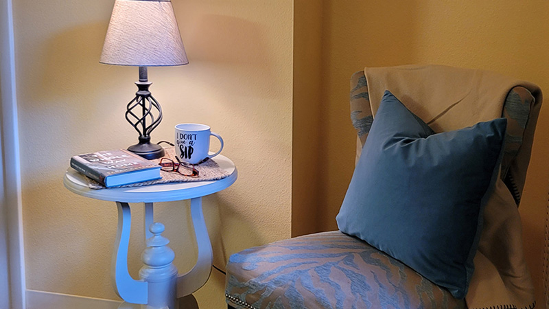 Chair with pillow next to end table with lamp and book